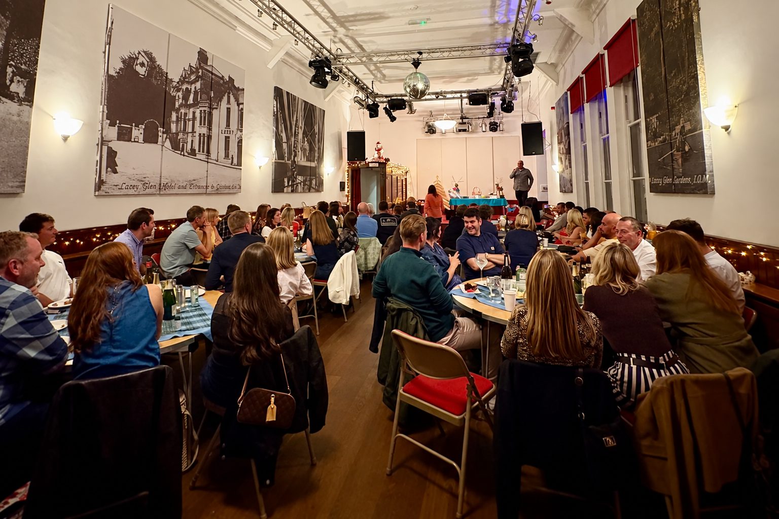 A full hall at the Mhelliah, with guests seated at tables and the stage lit at the far end